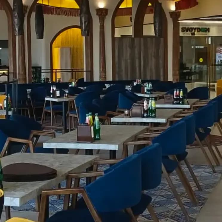 Современный ресторан с деревянными столами и синими креслами, украшенный арочными элементами.