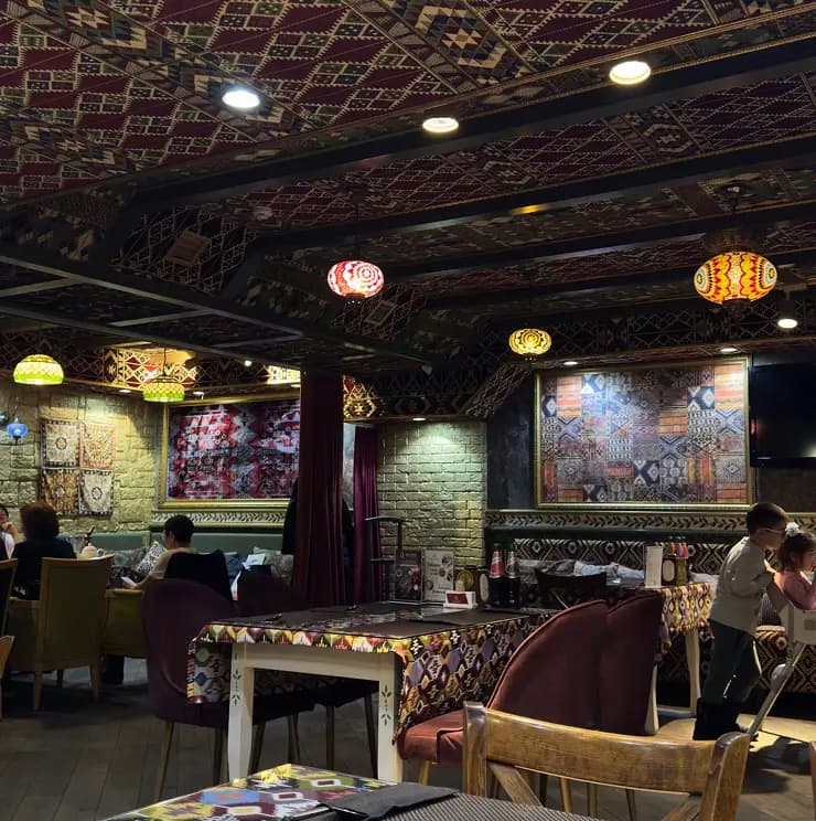 Атмосферный ресторан с восточным декором, коврами на стенах и потолке, яркими лампами и узорными скатертями.
