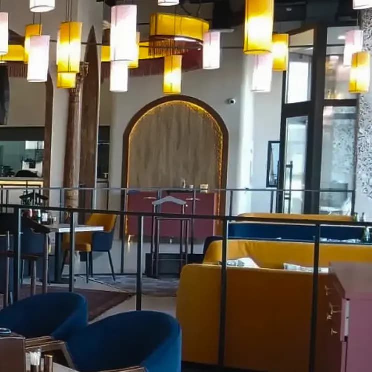 Интерьер ресторана с жёлтыми и синими диванами, подвесными светильниками и восточными элементами декора.