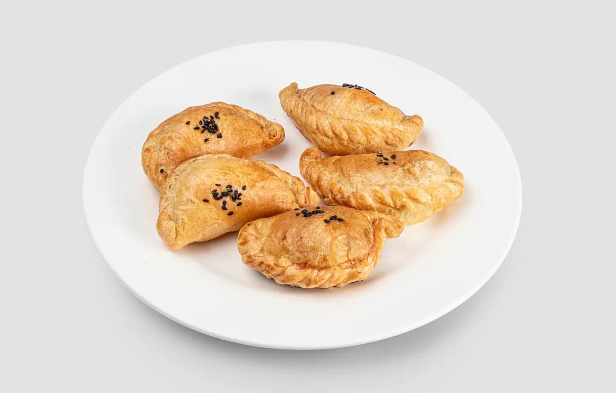 Пять мини самсы с чёрным кунжутом на белой тарелке.