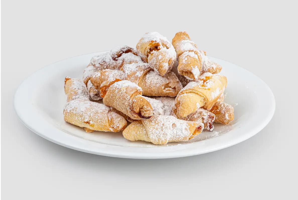Печенье-рулетики, посыпанные сахарной пудрой, на тарелке.
