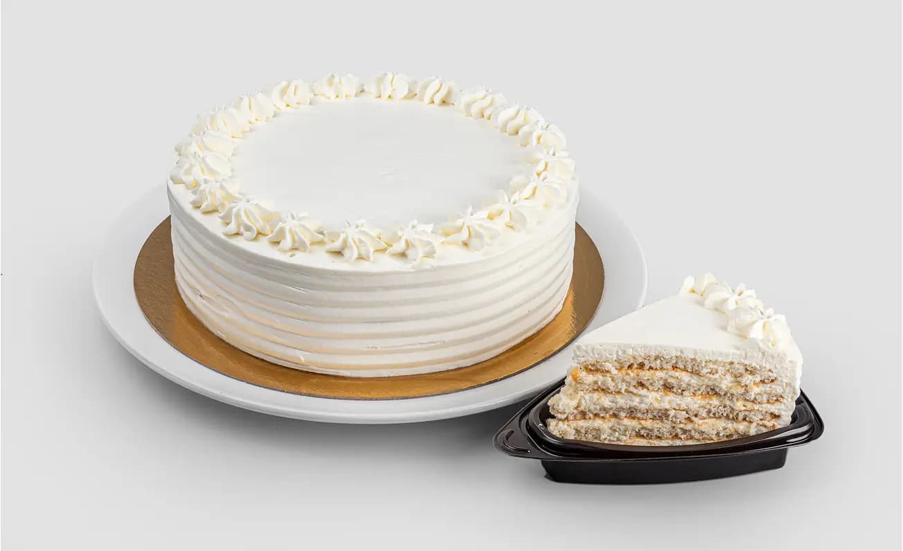 Белый слоёный торт с кремом, украшенный розетками, рядом кусочек торта.