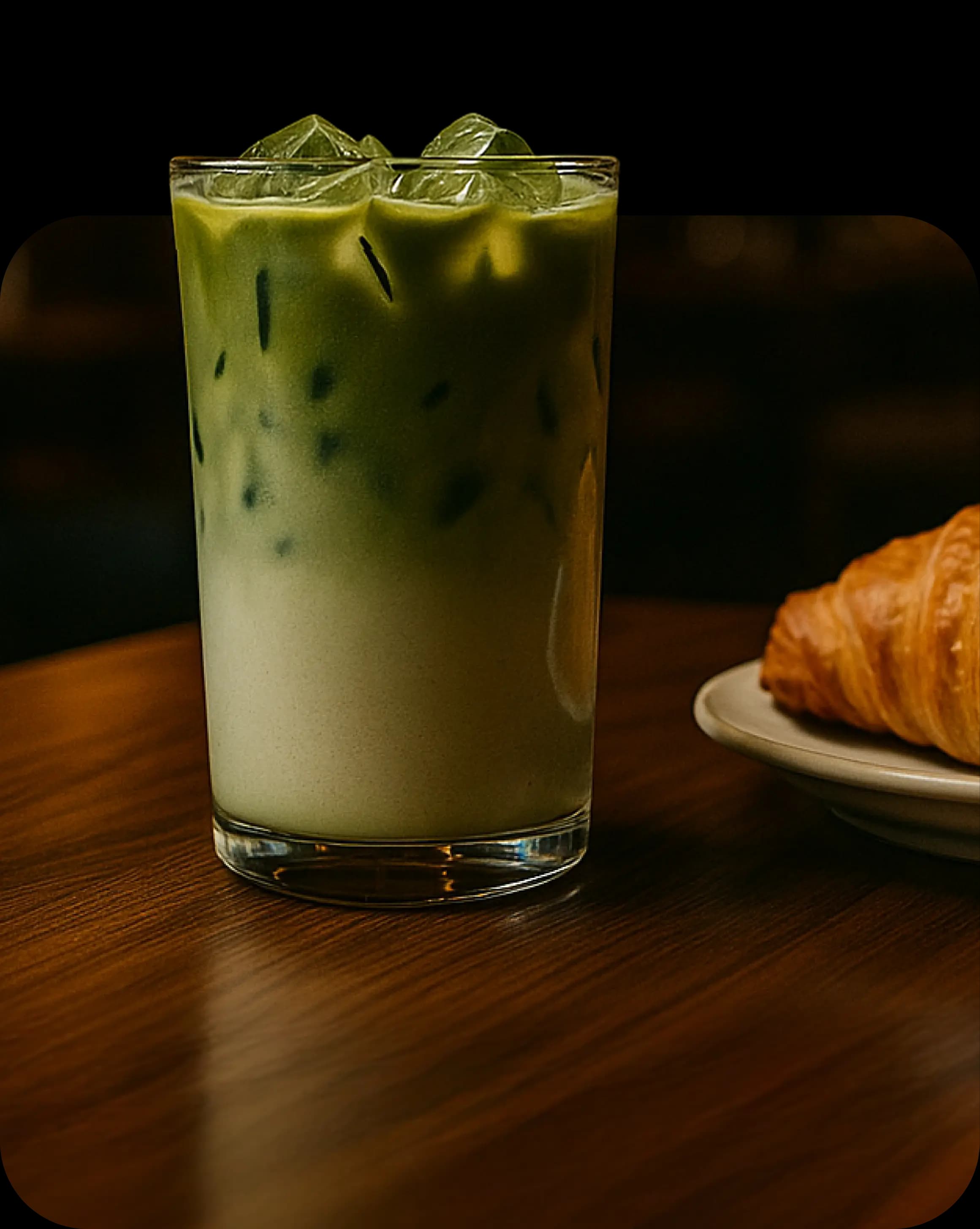 Рука держит ложку, из которой стекает соус на изысканно сервированное блюдо на тарелке, на фоне приглушённого интерьера и человека в белой рубашке.