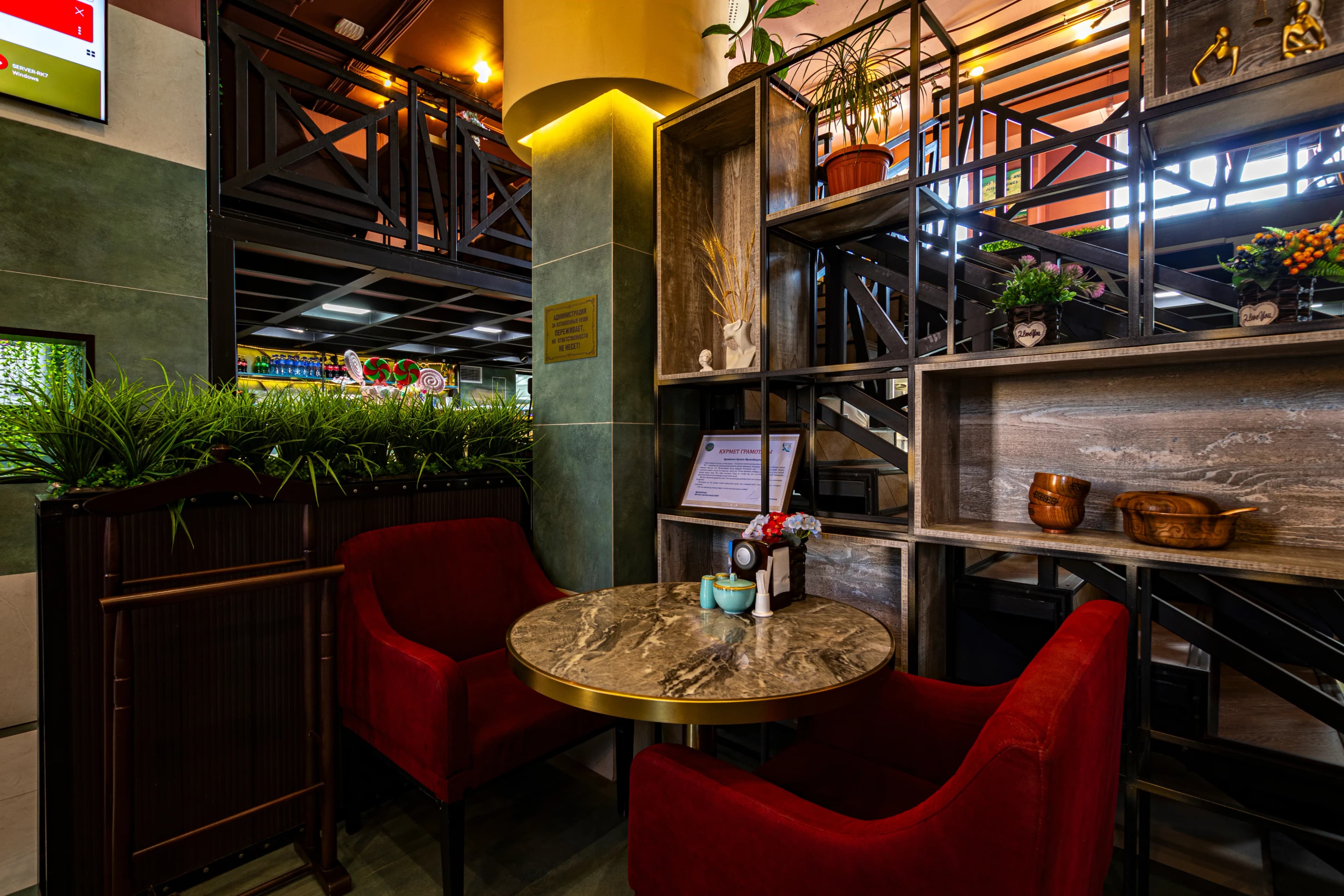 Уютный уголок кафе с круглым мраморным столиком и двумя красными креслами.