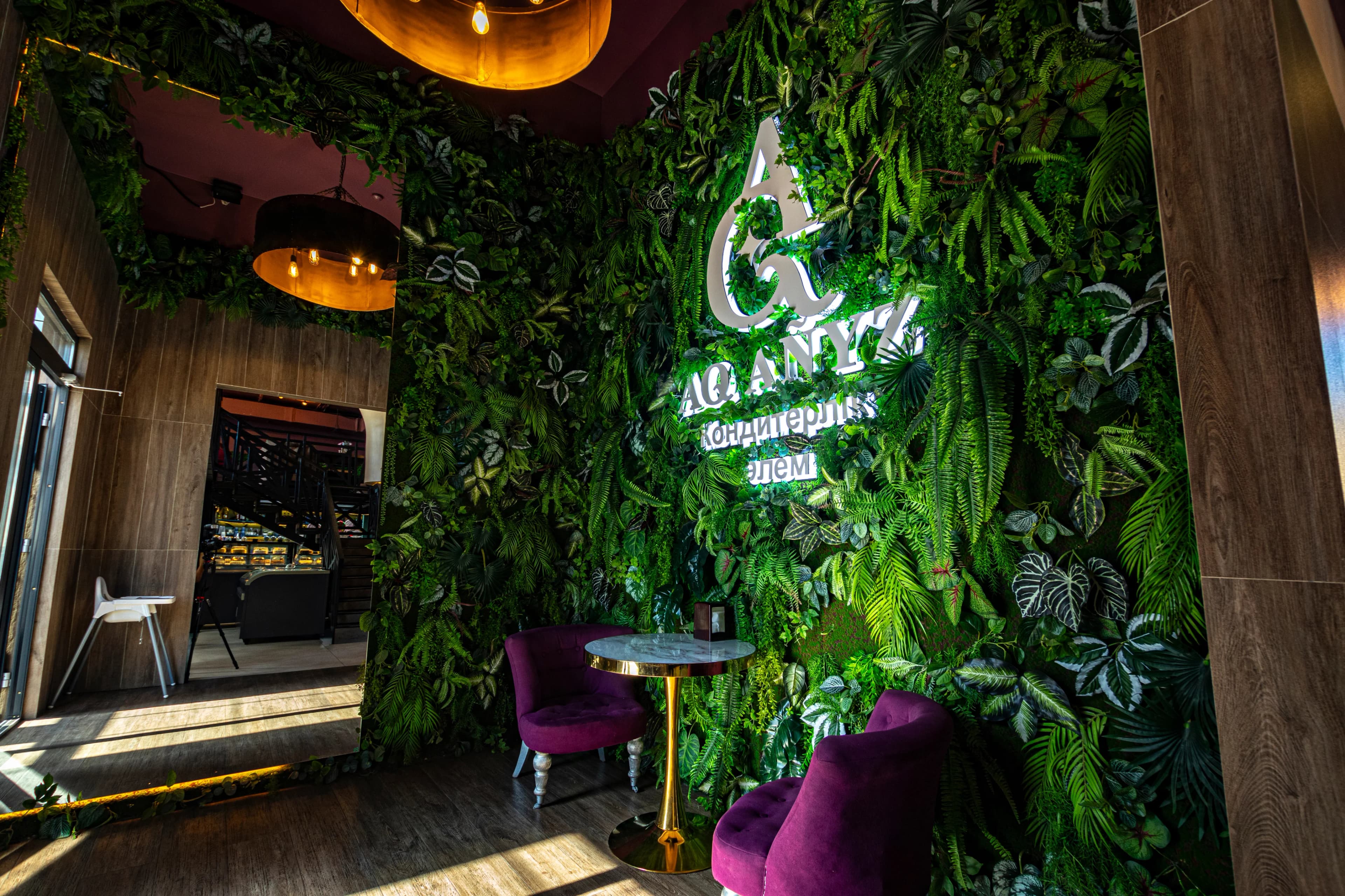 Интерьер кафе с яркой зелёной растительной стеной и логотипом AQ ANYZ.