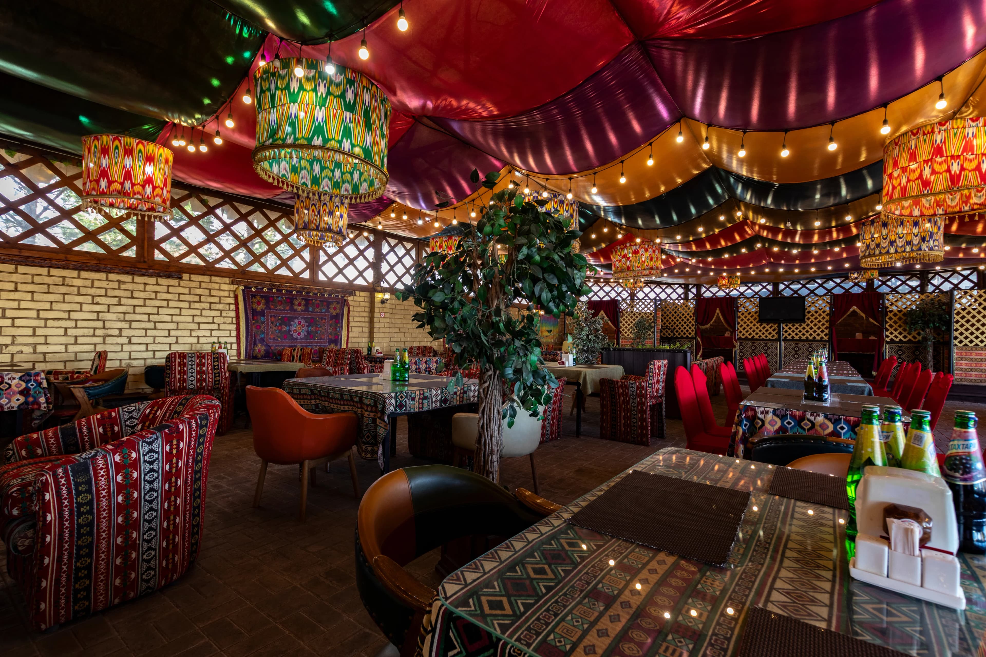 Восточный зал ресторана с яркими тканевыми потолками, гирляндами и узорными абажурами.