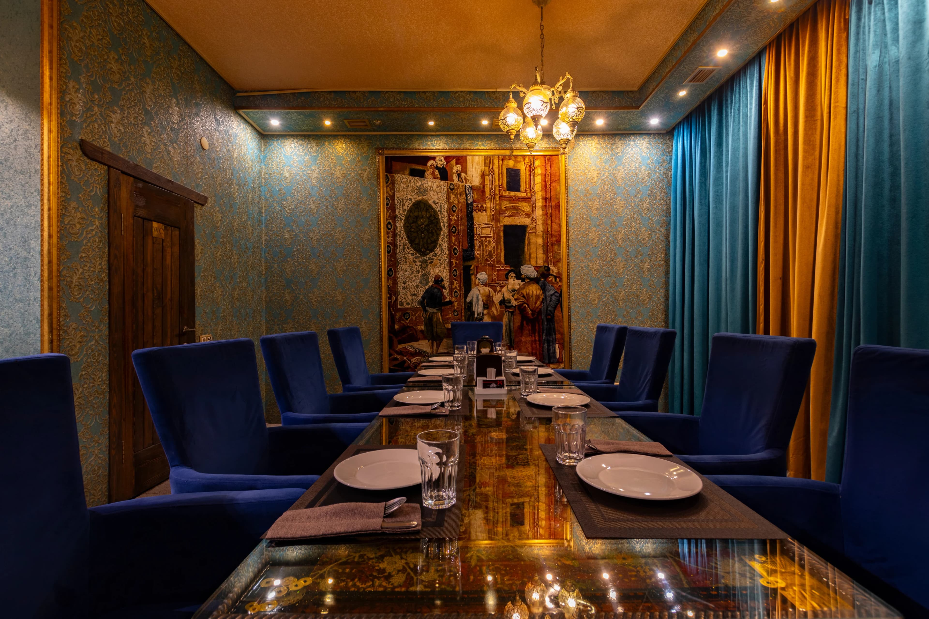 Закрытая комната ресторана с длинным столом, сервированным для ужина, и синими креслами.
